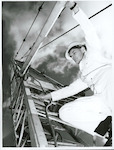 Title:
Government Service - Marine Deparatment

Publicity Caption:
Every contractor's crane on every new building in New Zealand must be surveyed and certified by a Marine Department engineer surveyor.  The Marine Department is short of engineers, and those who are on the job are among the hard-pressed in N.Z. today.  Here Mr A. Milton of Wellington reaches for the sky as he inspects a crane on a city project.

Photographer:
D. Nicholson.