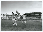 Title:
Sports - Soccer

Publicity Caption:
International Soccer, England v N.Z. Invitation XI at Basin Reserve, Wellington on June 2nd, 1969. The score was England 7 - N.Z. 1. N Z Goalkeeper, Derrick Phillips jumps high into the air to take the ball from off the head of England's high flying centre-forward, Tony Hateley while the N.Z. defence moves in to cover the goal

Photographer:
Mr R Coad
