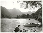 Title:
Fishing - Trout

Publicity Caption:
Mr. Peter Donaghy, a fishing guide with the Hollyford Tourist and Travel Co., tying a fresh fly on his line, two brown trout fresh from the Hollyford River are on the rocks in front of him. The Darran Mountains are in the background, Fiordland National Park. Otago

Photographer:
R. Anderson
