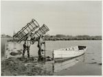Title: Commercial Eeling, Lake Ellesmere  Publicity Caption: A view of Lake Ellesmere as Mr. D. Vince (left) and W. Cunningham (right) wade out to their boat prior to setting the nets in the various deep water creeks.  June 1948  Photographer : Mr. Bigwood
