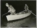 Title: Commercial Eeling, Lake Ellesmere  Publicity Caption: With torch and jag held at the ready, Wally Cunningham peers into the depths below for eels which he will jag and drag aboard.  The work of the boatman is exacting as he must be able to keep the boat steady and quiet.  June 1948  Photographer : Mr. Bigwood