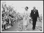 Queen Elizabeth and her guest walk on past the rows of flag-waving children, Palmerston North, 8 January 1954